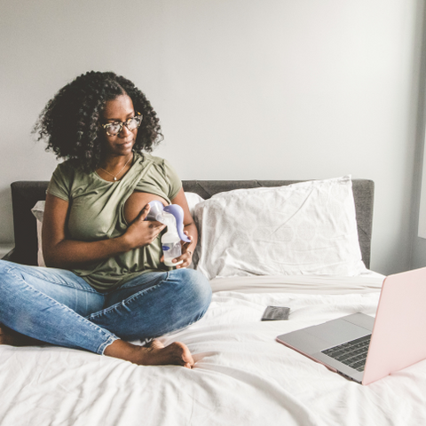 Mom sitting on bed using manual breast pump while working on her computer